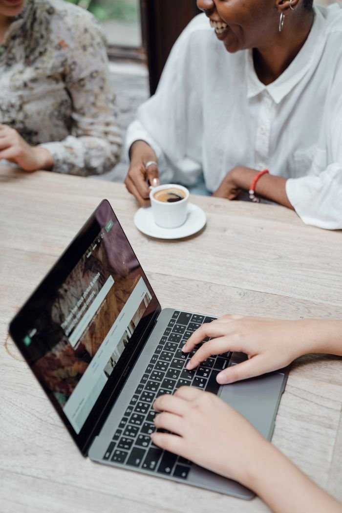 From above of crop anonymous female freelancer typing on laptop keyboard while sitting at table with diverse friends drinking coffee